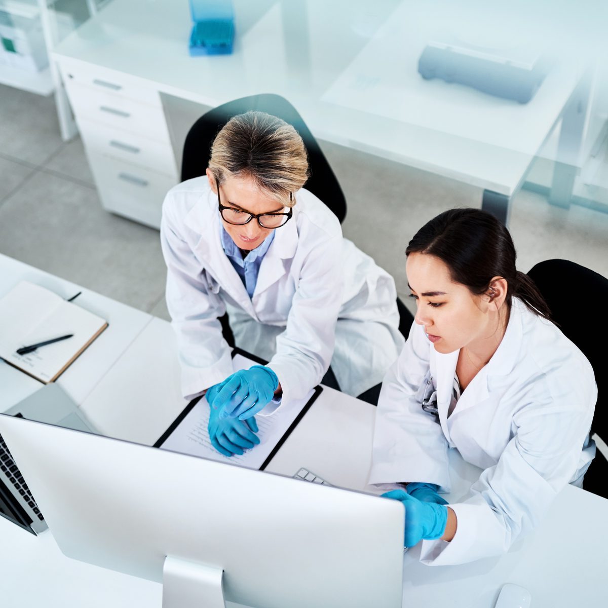 Two scientists in lab coats reviewing results together on a desktop monitor.